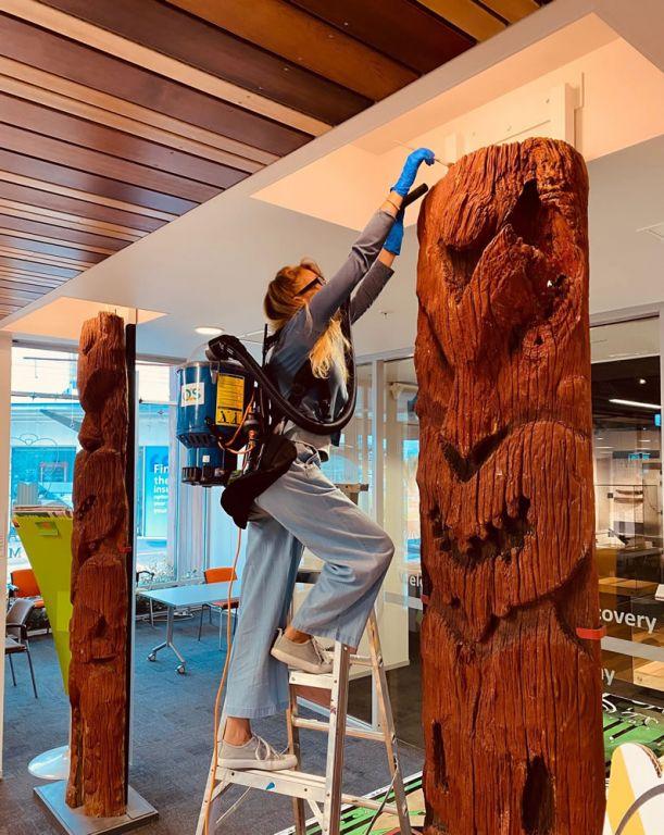 Valerie Noiret-Leblanc meticulously cares for the iconic amo (upright figures) as part of the Behind the Glass @ Te Kōputu project. Valerie Noiret-Leblanc and the iconic amo (upright figures)