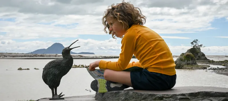 Kid sitting with Kiwi statue at the Heads