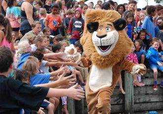 A lion mascot high-fives a group of children.